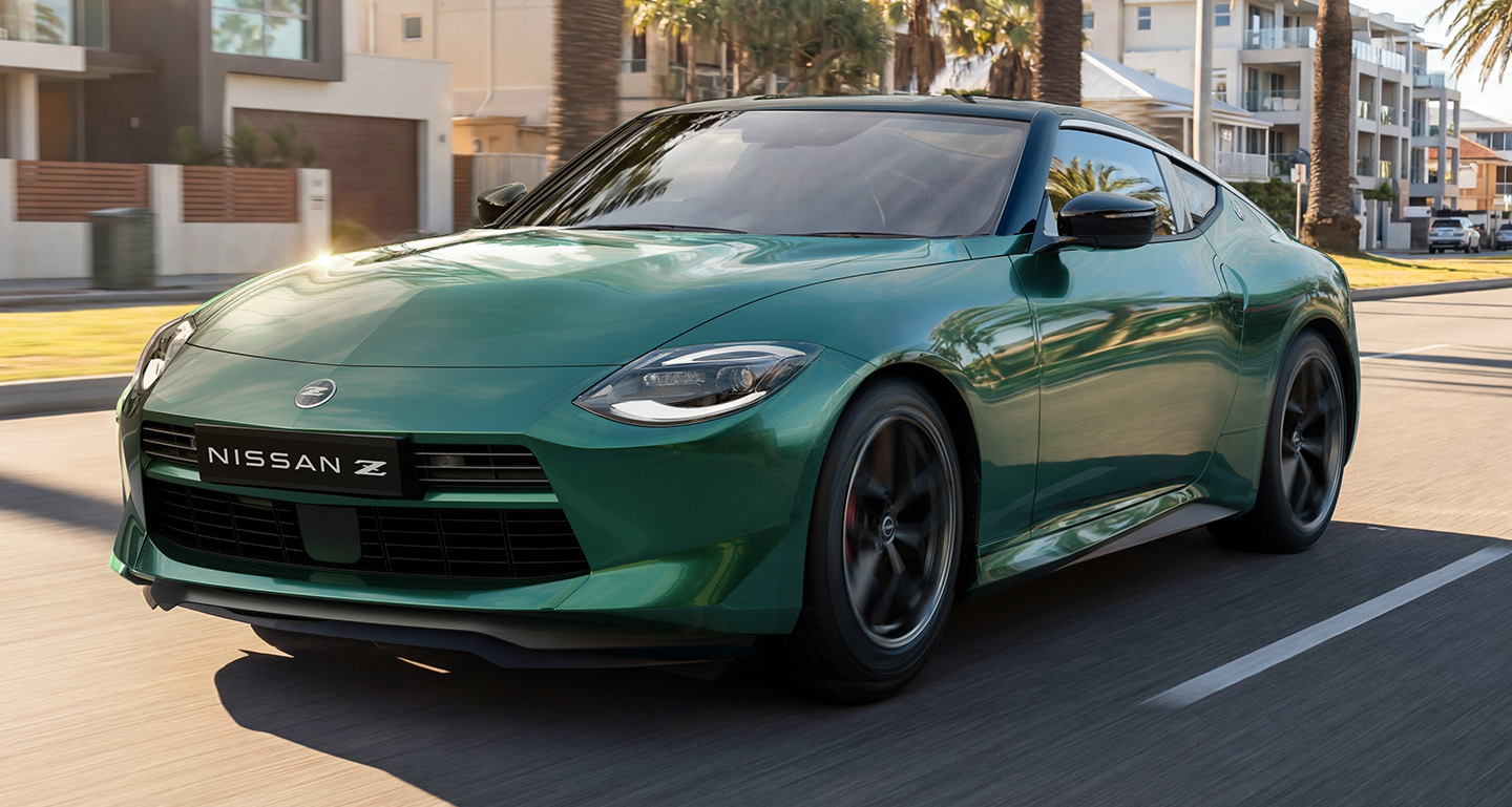 Green Nissan Z sports coupe driving along a palm-lined coastal street past modern beachside homes