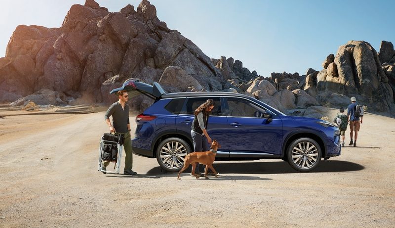 A family unloads a parked Nissan New X-TRAIL before heading onto a trail, with their dog beside them.
